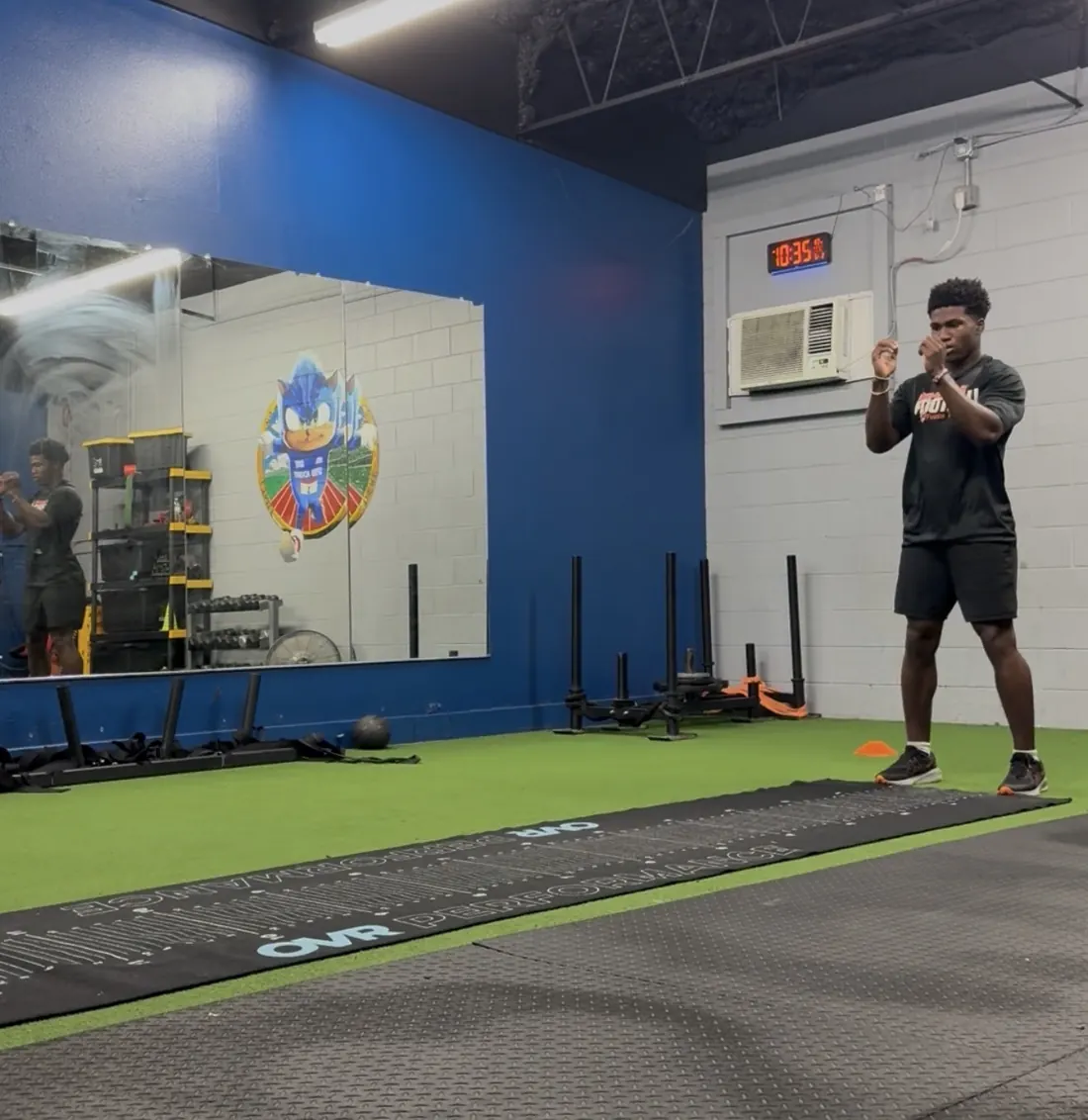 Coach watching an athlete train on the turf inside the Speed Academy gym